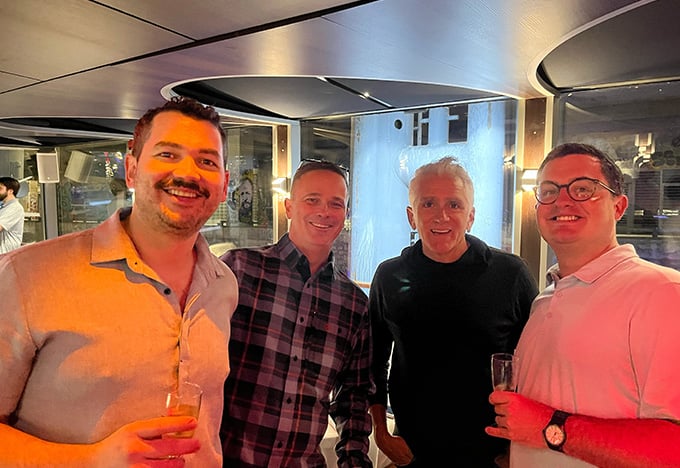 社交イベントで屋内に4人が寄り添い、それぞれ飲み物を手にしている。背景には温かみのある照明とモダンな装飾が映っている。