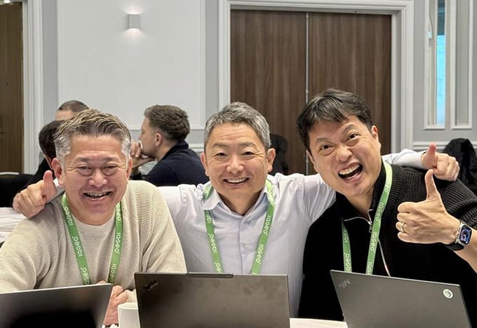 会議やワークショップ中に、3人がテーブルを囲んでノートパソコンを操作している。そのうち1人が親指を立てて「OK」の合図を送っている。