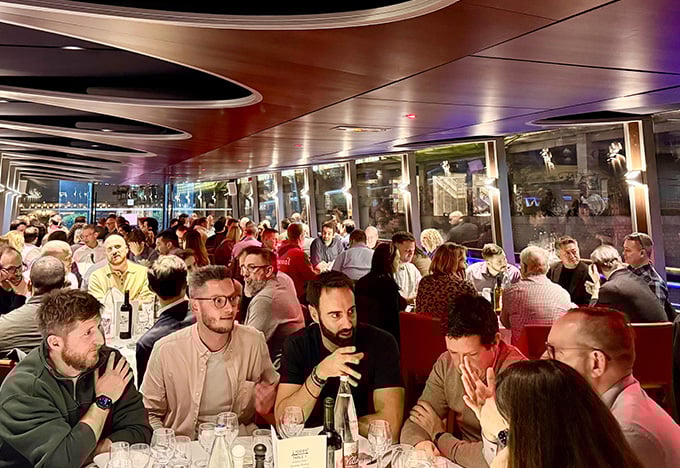 船上で行われた賑やかな夕食会で、大勢の人々がテーブルにぎっしりと座っている